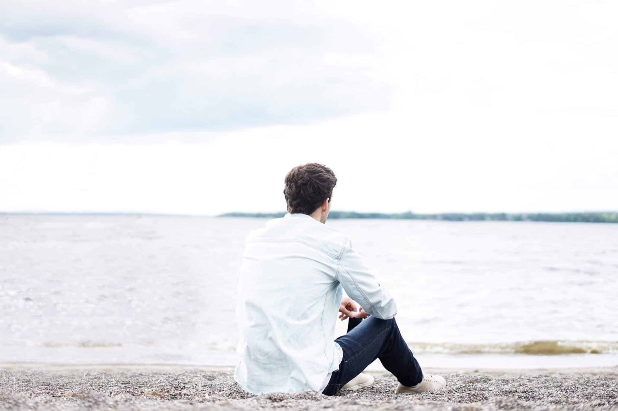 Man sitting on the beach looking out at the ocean.