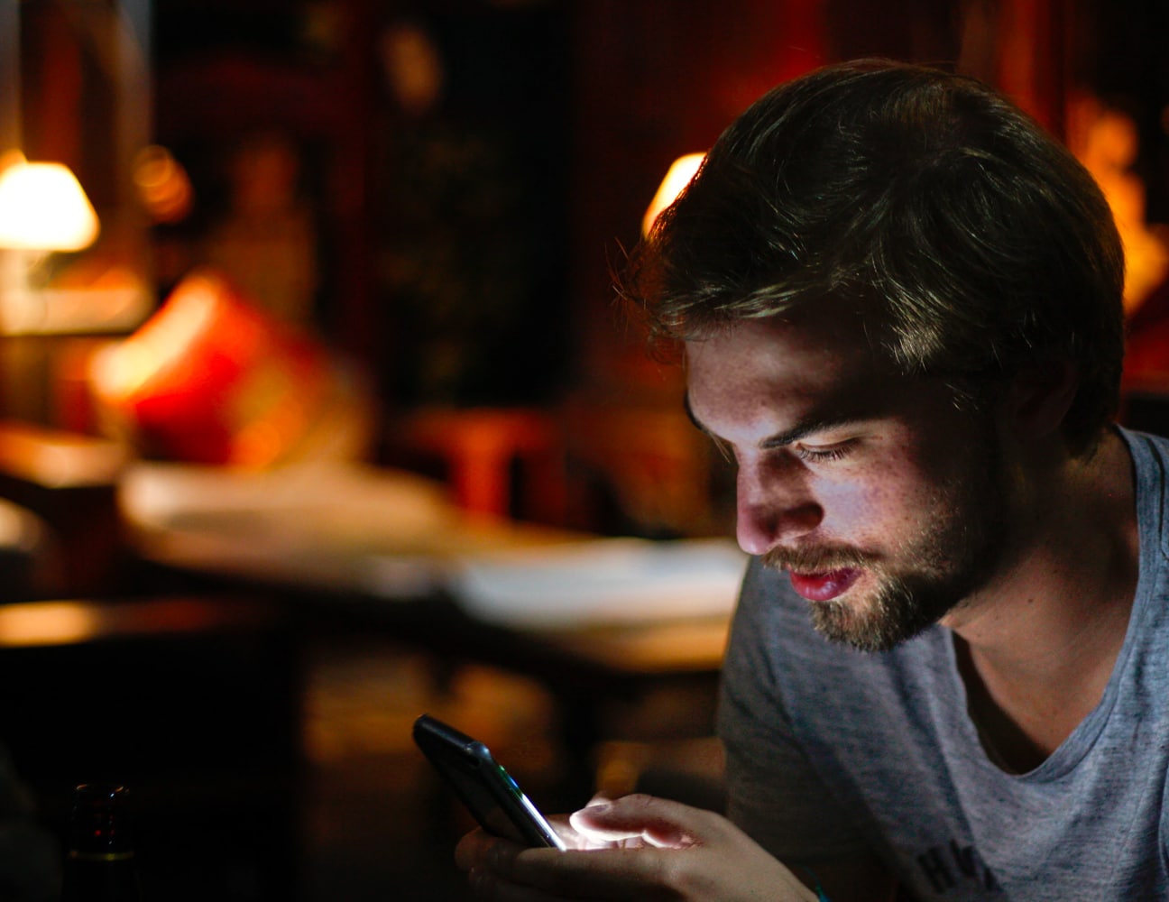 A guy scrolling on his smartphone in dim lighting.